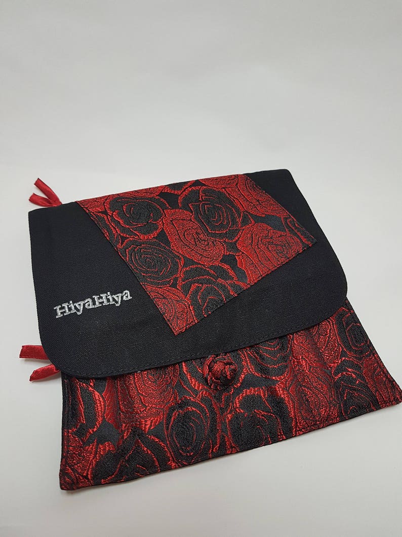 Puede incluir: Bolsa de tela negra con un patr&oacute;n de rosas rojas y el texto "HiyahHiya" bordado en la parte delantera.