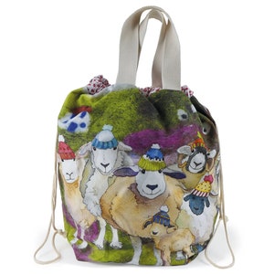 May include: A green canvas drawstring bag with a white handle. The bag features a colorful illustration of sheep wearing winter hats.