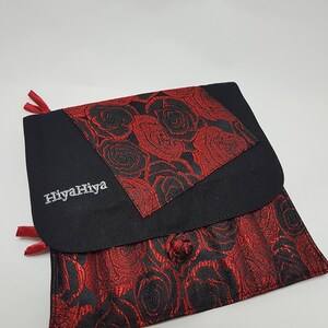 Puede incluir: Bolsa de tela negra con un patr&oacute;n de rosas rojas. La bolsa tiene una solapa con un patr&oacute;n de rosas rojas m&aacute;s peque&ntilde;o y el texto "HiyahHiya" bordado en blanco.