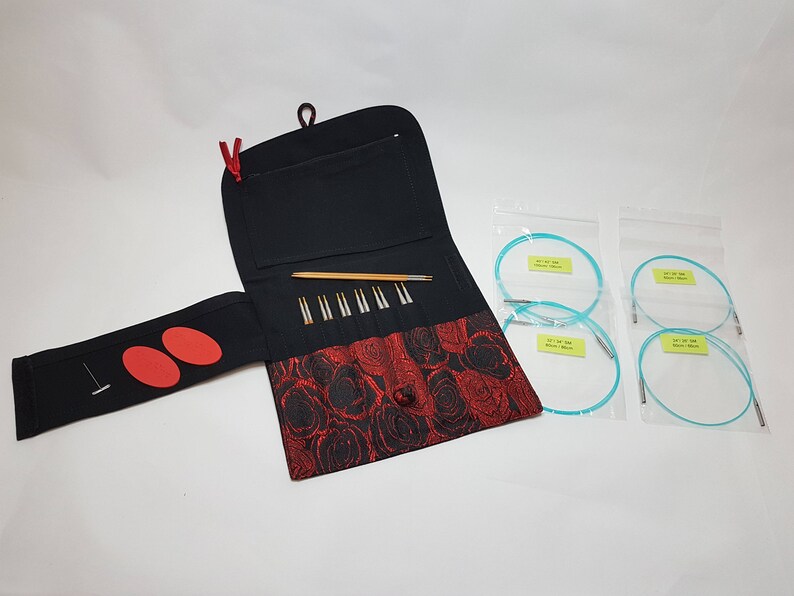 Puede incluir: Una funda de tela negra y roja con cierre de cremallera, que contiene un juego de agujas de tejer y un par de agujas circulares. Las agujas circulares est&aacute;n empaquetadas en bolsas de pl&aacute;stico transparentes.