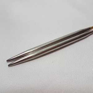 May include: Two silver knitting needles with gold tips.