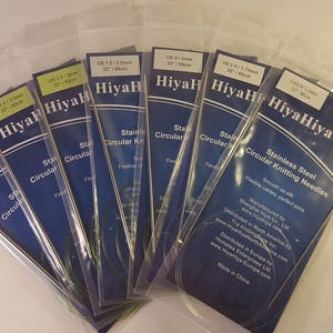 May include: A set of HiyaHiya stainless steel circular knitting needles in various sizes. The needles are packaged in clear plastic bags with blue and white labels. The labels include the size of the needles in US and mm, as well as the brand name HiyaHiya.