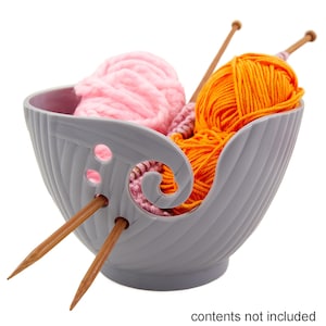 May include: A grey yarn bowl with two skeins of yarn, one pink and one orange, and two wooden knitting needles.