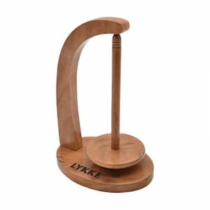 Op de afbeelding: Houten keukenrolhouder met een gebogen voet en een draaiende spil. De houder is gegraveerd met het woord "LYKKE".
