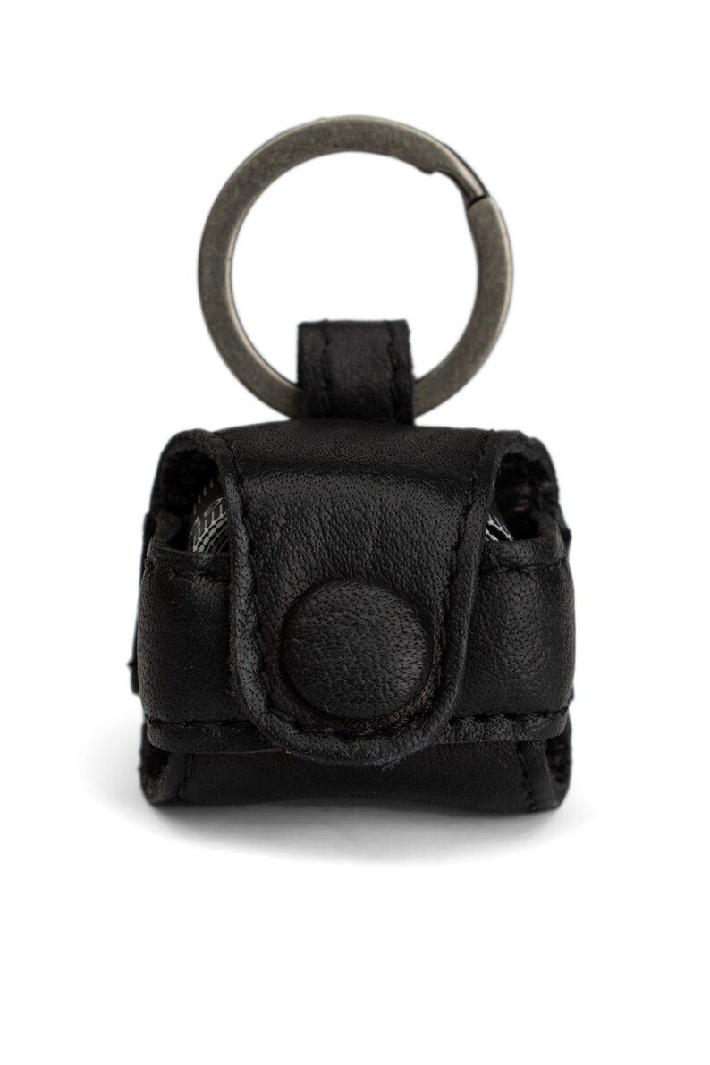 May include: A black leather keychain with a metal ring and a small flap closure. The keychain has a button on the front.