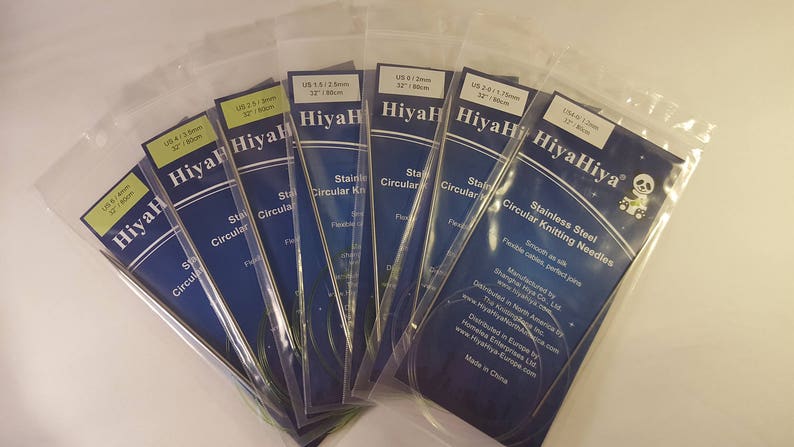 May include: A set of HiyaHiya stainless steel circular knitting needles in various sizes. The needles are packaged in clear plastic bags with blue and yellow labels. The labels include the size of the needles in US and metric measurements. The needles are smooth and flexible, perfect for knitting projects.