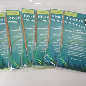 以下が含まれることがあります： さまざまなサイズが揃った、HiyaHiya 竹製輪針 6 本セット。針は天然竹製で、滑らかで柔軟性のあるケーブルが付いています。パッケージは緑と青のデザインで、HiyaHiya のロゴと製品情報が記載されています。