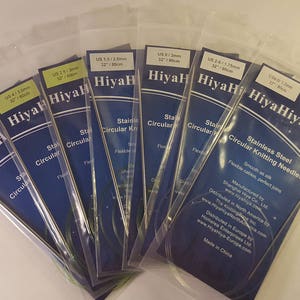 May include: A set of eight HiyaHiya stainless steel circular knitting needles in various sizes. The needles are packaged in clear plastic sleeves with blue and white labels. The labels include the size of the needles in US and metric measurements, as well as the brand name HiyaHiya.