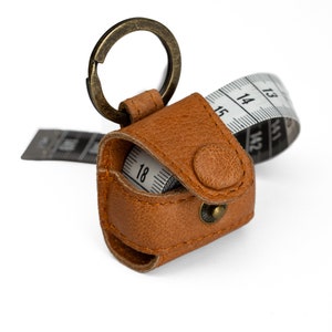 May include: A brown leather keychain with a retractable tape measure. The tape measure is partially extended and shows the numbers 12, 13, 14, 15, 16, 17, and 18.