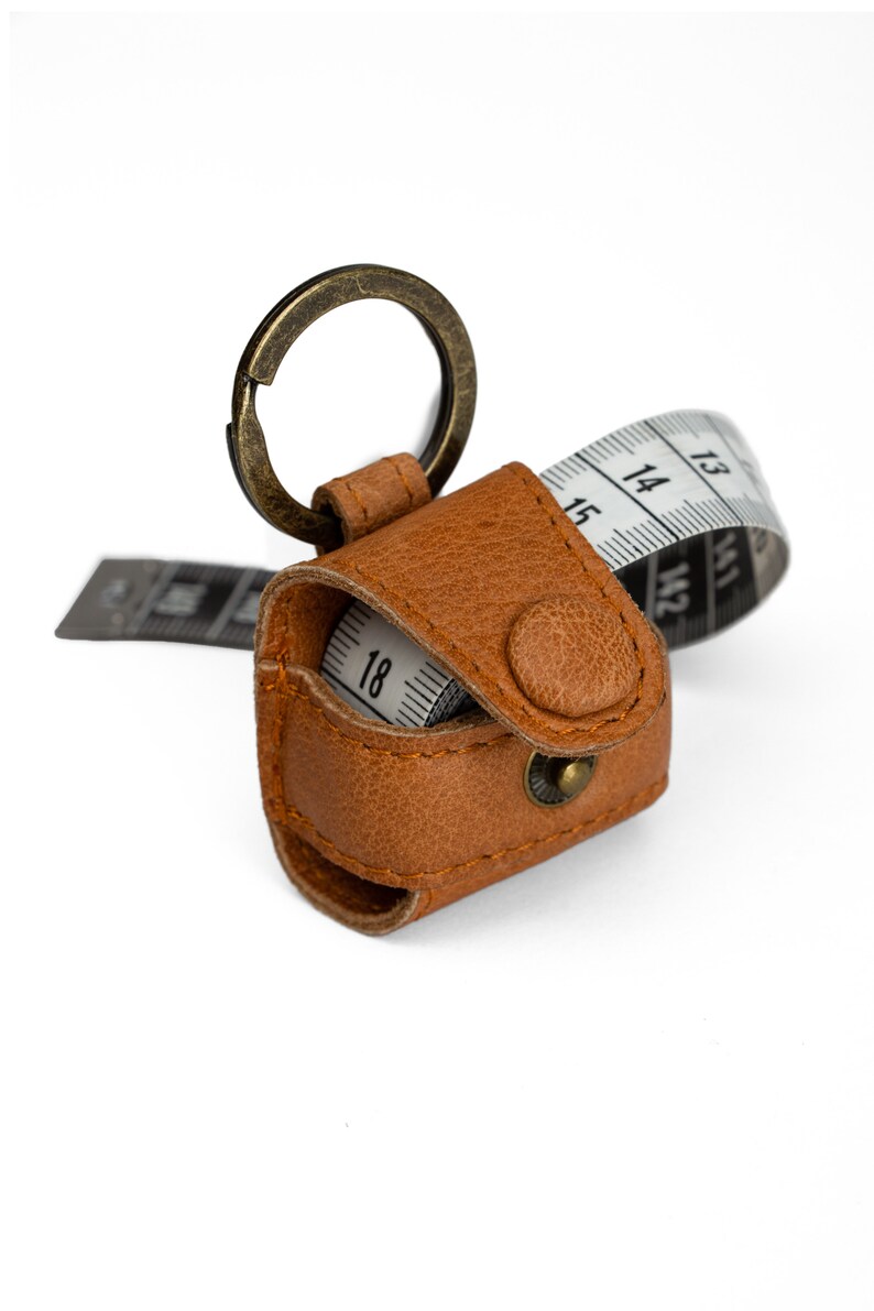 May include: A brown leather keychain with a retractable tape measure. The tape measure is partially extended and shows the numbers 12, 13, 14, 15, 16, 17, and 18.