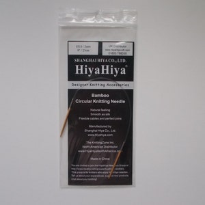 May include: A close-up of a HiyaHiya Bamboo Circular Knitting Needle in a plastic package. The needle is 9 inches (23 cm) long and is made of natural bamboo. The package includes the brand name HiyaHiya and the text "Designer Knitting Accessories".