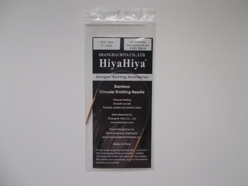 May include: A close-up of a HiyaHiya Bamboo Circular Knitting Needle in a plastic package. The needle is 9 inches (23 cm) long and is made of natural bamboo. The package includes the brand name HiyaHiya and the text "Designer Knitting Accessories".