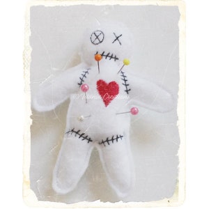May include: White felt voodoo doll with black stitching, red heart, and colourful pins. The doll has an X for eyes and a stitched mouth.