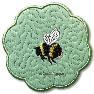May include: An embroidered coaster in light green, with a scalloped edge. It features a bumblebee with black and yellow stripes and white wings. The design includes a stitched, swirling pattern and the text "©Titania Creations".