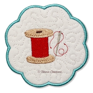 May include: Embroidered patch featuring a red spool of thread with a needle and thread, set against a white background with a quilted pattern. The patch has a scalloped edge in teal. The text "Titania Creations" is at the bottom.