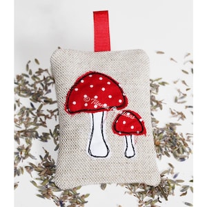 May include: A small linen pouch with a red ribbon loop, decorated with two embroidered red and white mushrooms. The pouch is filled with dried lavender.