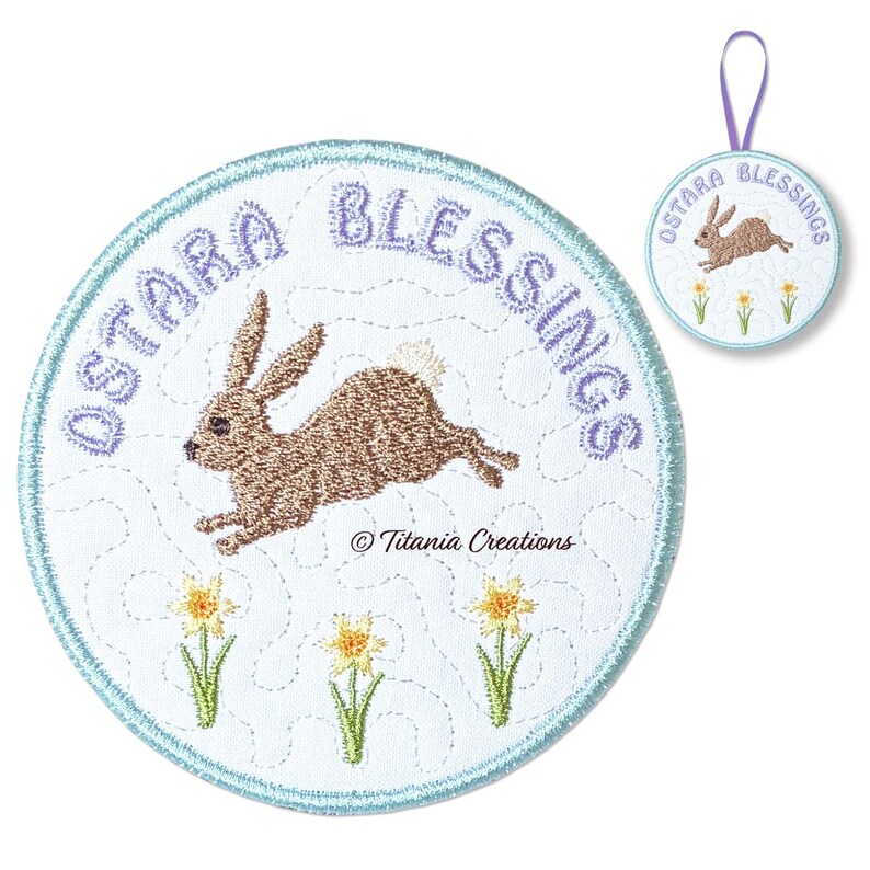 Może przedstawiać: Haftowana okrągła naszywka z napisem "OSTARA BLESSINGS" w jasnofioletowym kolorze. Brązowy kr&oacute;lik skacze na białym tle, z trzema ż&oacute;łtymi żonkilami na dole. Mniejsza wersja z fioletową pętlą jest r&oacute;wnież pokazana.