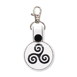 May include: White leather keychain with a black metal clasp and a round white leather tag with a black embroidered Celtic knot design.