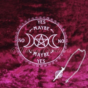 Puede incluir: Un tablero de péndulo bordado en blanco con un pentagrama y un símbolo de triple luna sobre una superficie de terciopelo rojo oscuro. El tablero tiene las palabras "YES", "MAYBE" y "NO" escritas alrededor del borde. Un péndulo de cristal con una cadena plateada cuelga sobre el tablero.