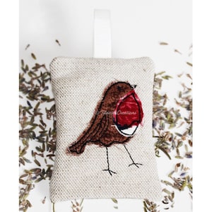 May include: A small, beige linen sachet with a red-breasted robin embroidered on it. The sachet is filled with dried lavender and has a white ribbon loop for hanging.