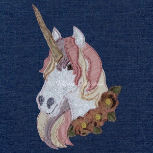 May include: A white unicorn head with a pink and beige mane and horn, embroidered with a floral garland of brown and green flowers.