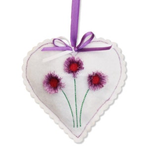 May include: White felt heart-shaped ornament with three purple and red embroidered flowers and green stems. A purple ribbon is attached to the top.