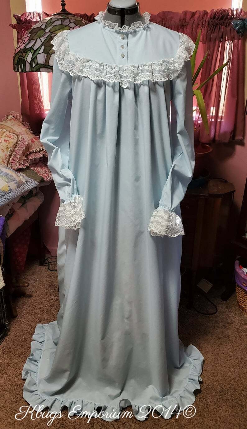 Puede incluir: Un camis&oacute;n azul claro con ribete de encaje blanco alrededor del cuello, las mu&ntilde;ecas y el dobladillo. El camis&oacute;n tiene un frente abotonado y un corpi&ntilde;o fruncido.