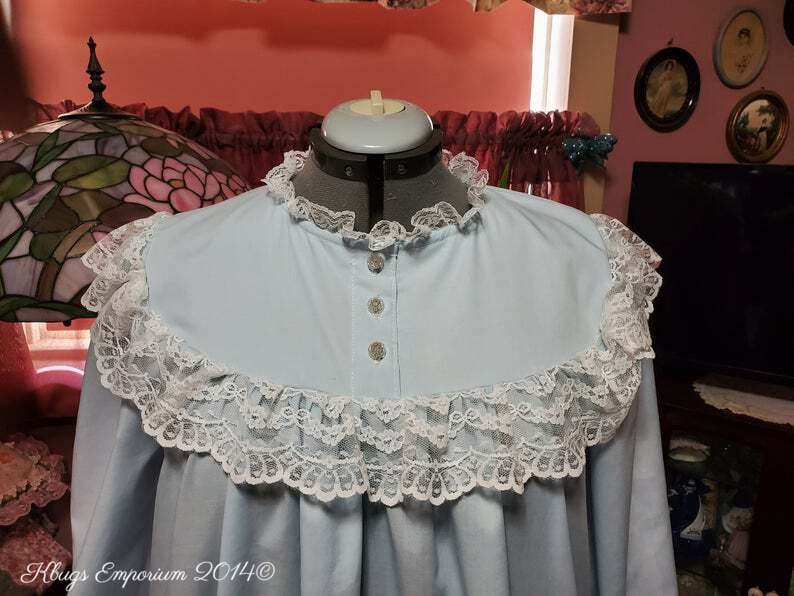 Puede incluir: Un camis&oacute;n azul claro con un ribete de encaje blanco alrededor del cuello y las mangas. El camis&oacute;n tiene un frente abotonado.