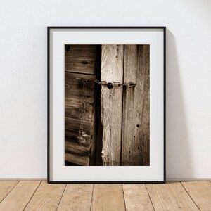 May include: A close-up of a weathered wooden door secured with a rusty chain and padlock. The wood is a warm brown color and shows signs of age and wear.
