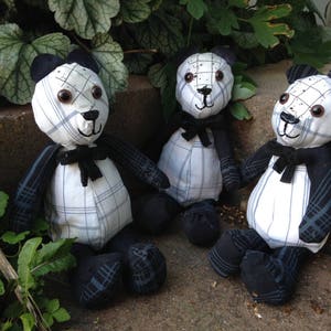 Könnte beinhalten: Drei handgefertigte Plüsch-Pandabären aus schwarzem und weißem kariertem Stoff. Die Bären sitzen auf einer Steinoberfläche mit grünen Pflanzen im Hintergrund.
