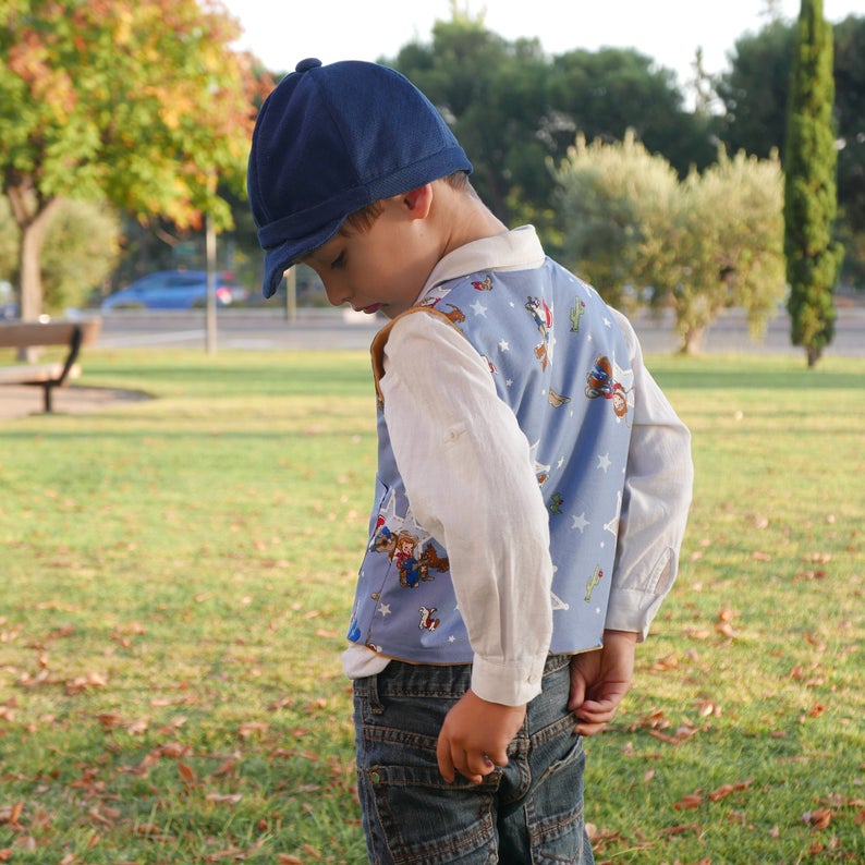 Puede incluir: Un ni&ntilde;o peque&ntilde;o con un chaleco estampado en azul y blanco con una gorra azul marino. El chaleco tiene un patr&oacute;n de estrellas y presenta personajes de dibujos animados.