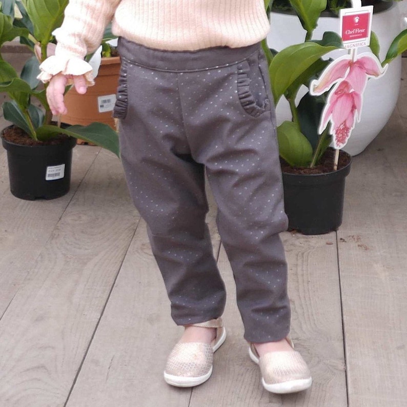 May include: A child wearing gray pants with white polka dots and gold shoes. The pants have a ruffled detail on the pockets.