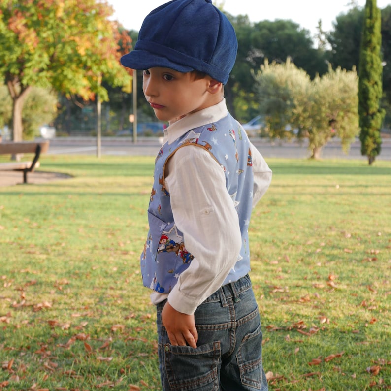 Puede incluir: Una persona joven que lleva un chaleco estampado en azul y blanco, una camisa blanca y pantalones vaqueros azules. Lleva una gorra de repartidor de peri&oacute;dicos azul oscuro.