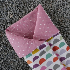 K&ouml;nnte beinhalten: Ein rosa-wei&szlig;er Schlafsack mit einem geometrischen Muster aus bunten Halbkreisen. Der Schlafsack ist in der H&auml;lfte gefaltet und hat ein rosa-wei&szlig;es gemustertes Futter.