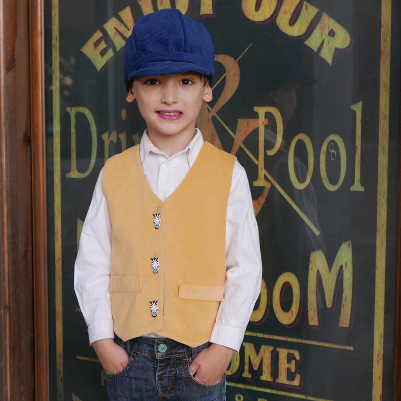 Puede incluir: Una persona joven que lleva un chaleco amarillo con botones de estampado de cebra, una camisa blanca, pantalones vaqueros azules y una gorra de newsboy azul. La persona est&aacute; de pie frente a un cartel que dice "Enjoy Our Drink & Pool Room".