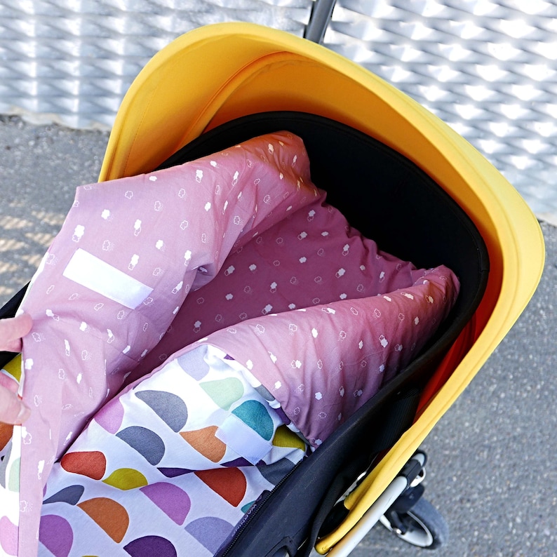 K&ouml;nnte beinhalten: Ein gelber Kinderwagen mit einem schwarzen Verdeck und einer rosa-wei&szlig;en gemusterten Innenausstattung. Die Innenausstattung ist umgeklappt und hat eine wei&szlig;e und bunte gemusterte Schicht darunter.