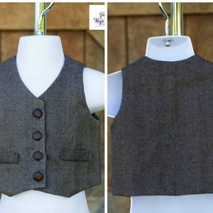 Puede incluir: Un chaleco de tweed marr&oacute;n con cuatro botones marrones y dos bolsillos. El chaleco est&aacute; en un maniqu&iacute; blanco.
