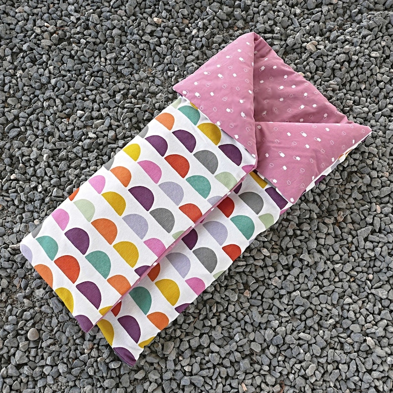 K&ouml;nnte beinhalten: Ein rosa-gr&uuml;ner Schlafsack mit einem geometrischen Muster aus Halbkreisen. Der Schlafsack ist aus weichem Stoff gefertigt und perfekt f&uuml;r ein Kind.