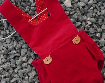 May include: Red corduroy baby overall with a white polka dot lining and two wooden cat buttons.
