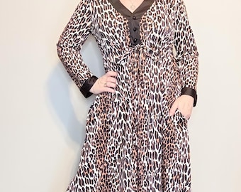 May include: A long-sleeved maxi dress featuring a brown, black, and white leopard print pattern. The dress includes a solid black V-neck collar, black cuffs, a button-down placket at the chest, and two side pockets integrated into the skirt.
