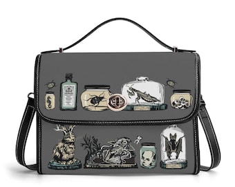 May include: A grey handbag with a top handle and a black trim, featuring a graphic print of various curiosities including jars with insects, a seahorse, a skull, a rabbit, a mermaid skeleton, a doll head, and a bat inside a glass dome.