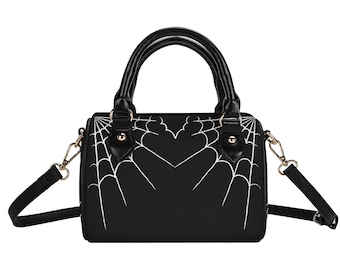 May include: A black handbag featuring a white spiderweb pattern on the front panel. The bag has two top handles, gold-toned metal hardware, and a detachable shoulder strap. The web design converges toward the center, forming a heart shape.