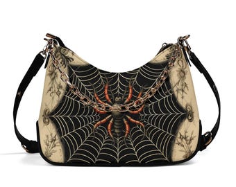 May include: A hobo-style shoulder bag featuring a central graphic of a spider on a web against a black background, flanked by cream-colored panels with botanical illustrations. The bag includes a gold-tone metal chain strap and black side straps.