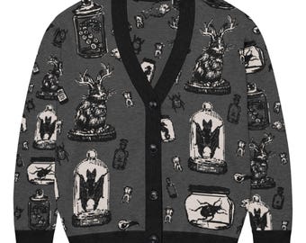 May include: A charcoal gray V-neck cardigan featuring a repeating black and white graphic print of jackalopes, bats in glass cloches, insects in jars, and small bottles. The garment has a solid black ribbed trim along the neckline, cuffs, and hem.