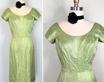 May include: A light green dress with a textured floral pattern, short sleeves, and a wide scoop neckline. The dress is displayed on a mannequin wearing a black velvet choker with a large black fabric flower accent at the center of the neck.