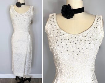 May include: A sleeveless white dress featuring a textured swirl pattern and small silver-toned embellishments across the bodice. The dress is displayed on a mannequin wearing a black velvet choker with a large black fabric flower accent.
