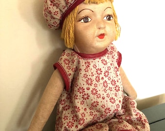 May include: A vintage cloth doll with blonde yarn hair, wearing a red and white floral dress and a red and white floral hat.