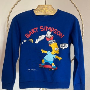 Könnte beinhalten: Blauer Pullover mit einem Aufdruck von Bart Simpson beim Skateboarden und dem Text "BART SIMPSON" und "WHOA, MAMA!" auf der Vorderseite.