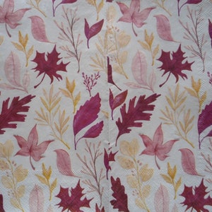 May include: A white paper napkin with a repeating pattern of autumn leaves and branches in shades of burgundy, pink, and yellow. The leaves are stylized and arranged in a scattered design, creating a seasonal theme.