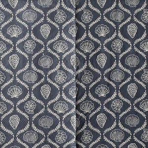 May include: A navy blue fabric with a repeating pattern of white seashells, oyster shells, and floral elements. The design is arranged in a diamond lattice, creating a nautical or coastal theme. The fabric appears to be a decorative textile.